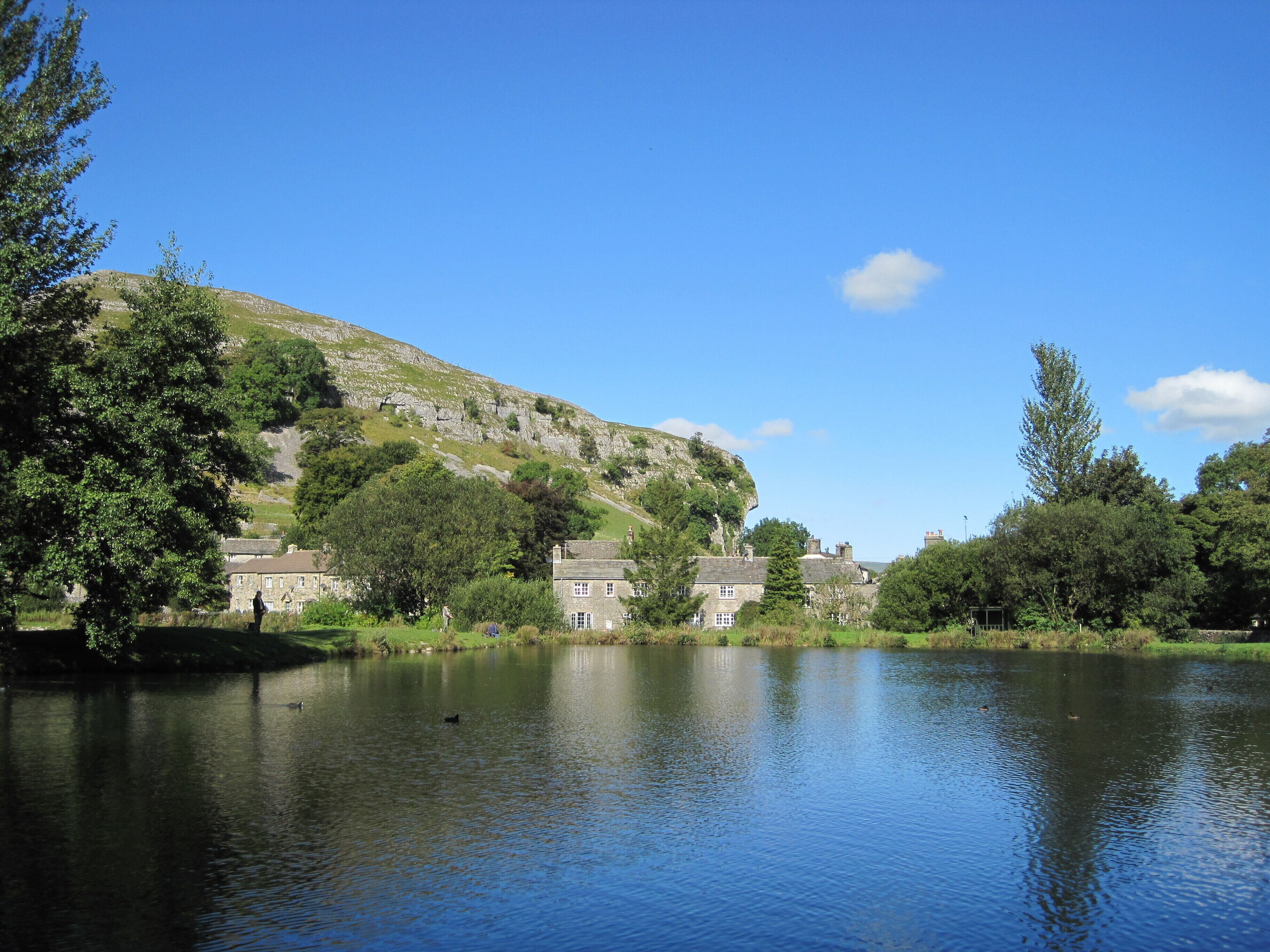 A calm lake with a stone bridge, surrounded by lush greenery and historic stone buildings.