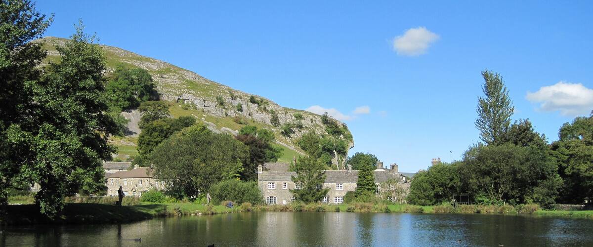 A calm lake with a stone bridge, surrounded by lush greenery and historic stone buildings.