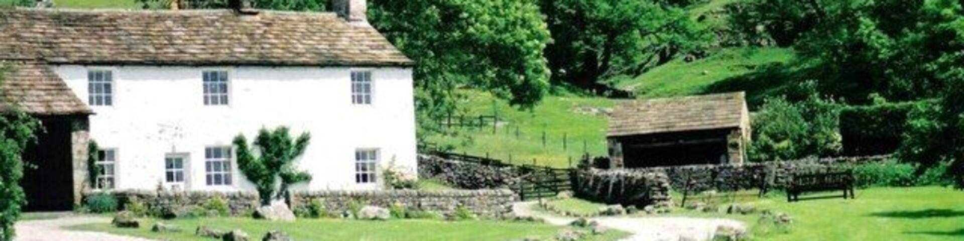 A white house with a stone pathway leading to it, surrounded by lush green hills and trees.