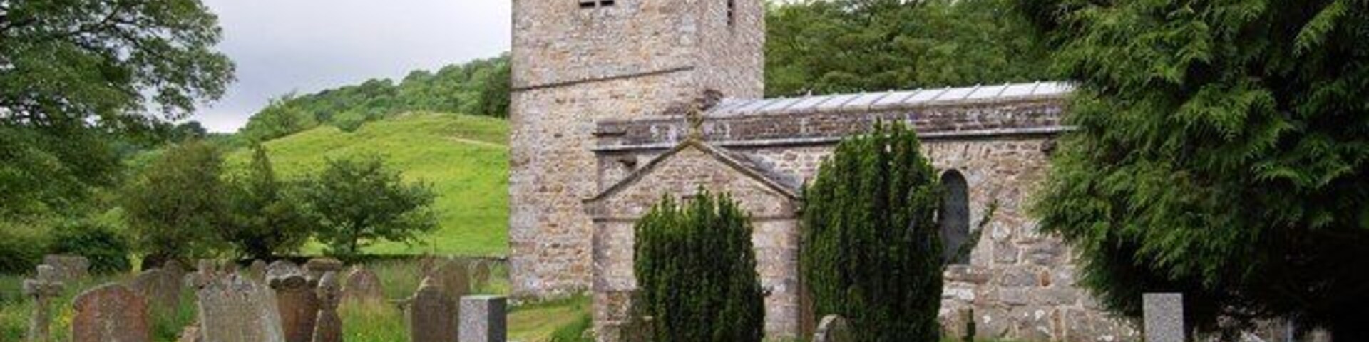 Una iglesia de piedra histórica con una torre, rodeada por un cementerio de lápidas.