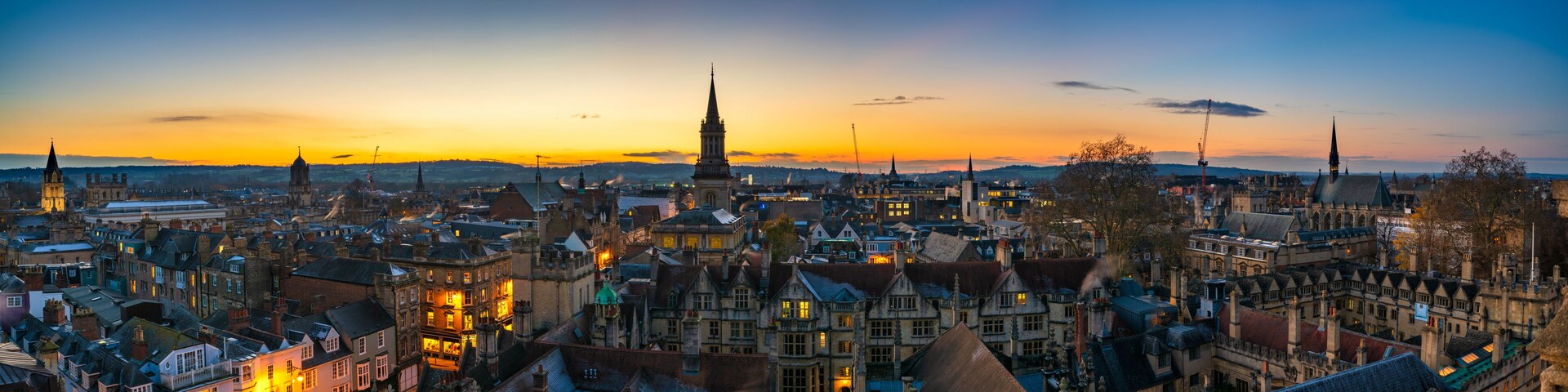 Un paisaje urbano al atardecer con edificios históricos y una imponente aguja de iglesia.