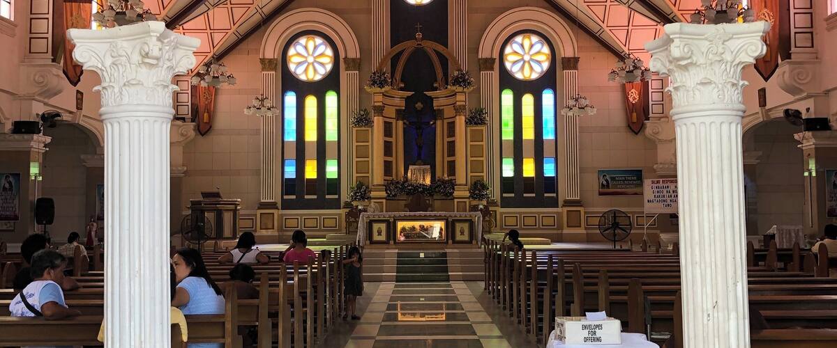 A church interior with a checkered floor, white columns, and stained glass windows.