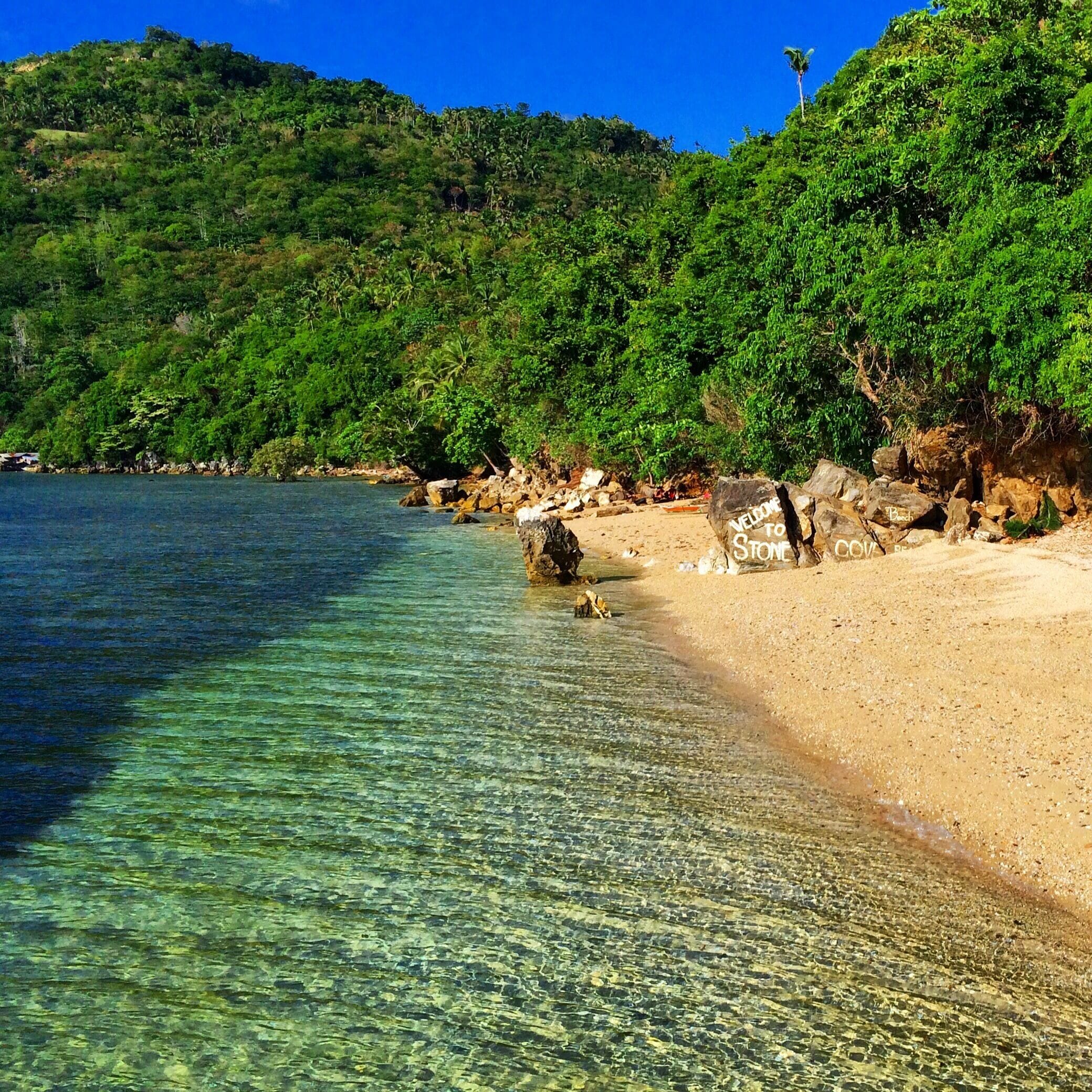 A clear beach with a welcoming sign, surrounded by lush green hills.