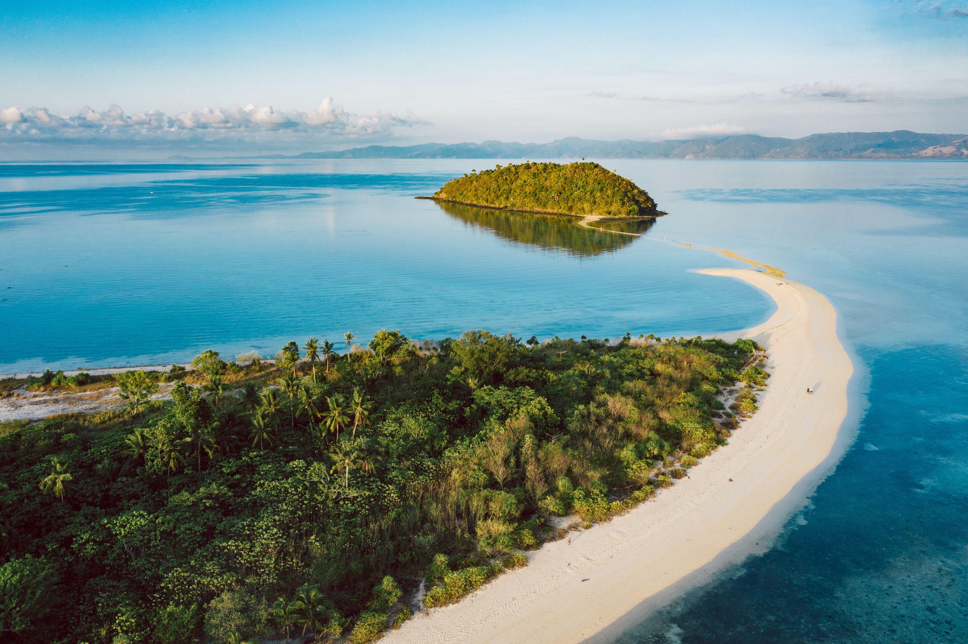 A tropical island surrounded by clear blue waters, a sandy beach, and dense green vegetation.