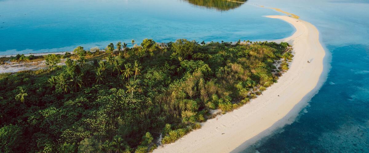 A tropical island surrounded by clear blue waters, a sandy beach, and dense green vegetation.