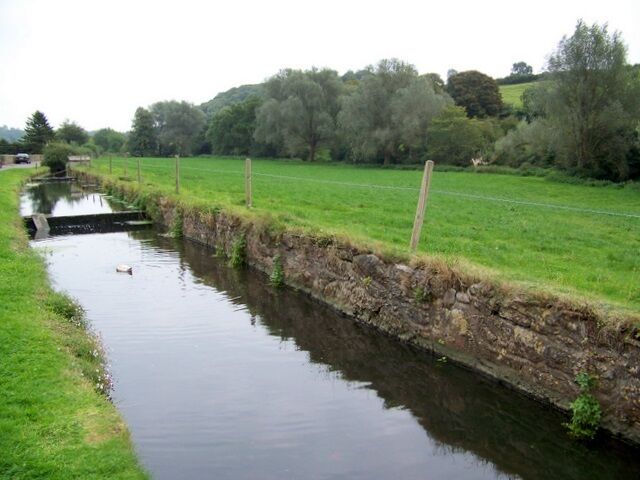 A narrow water channel with a stone wall on one side and a grassy field on the other.
