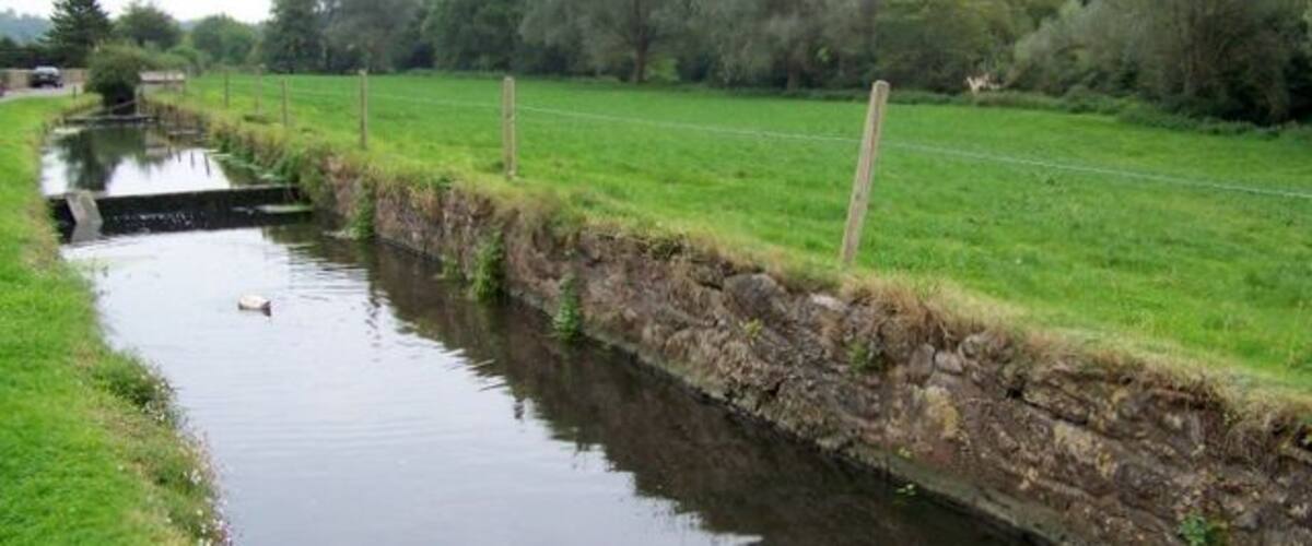 A narrow water channel with a stone wall on one side and a grassy field on the other.