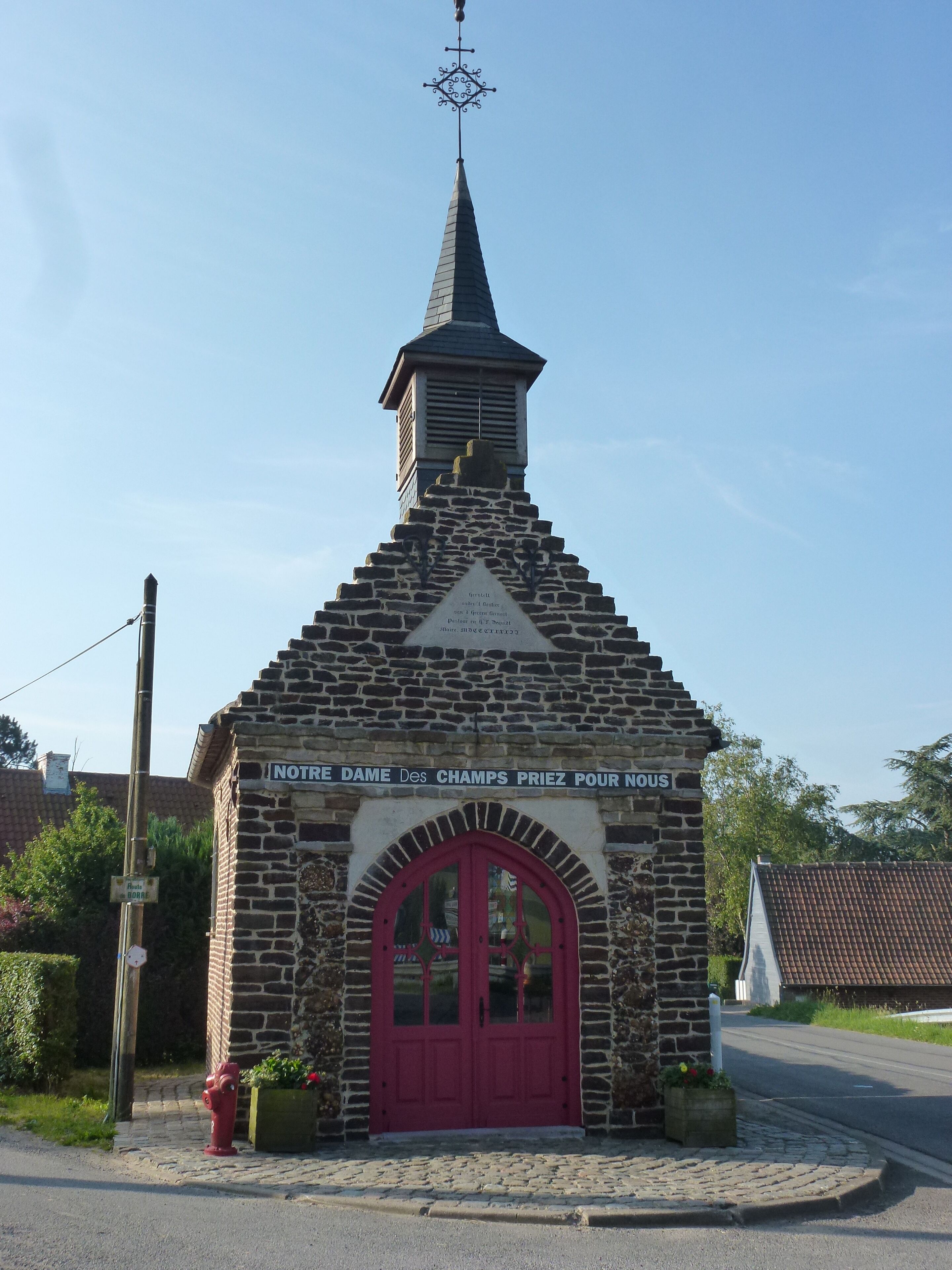 A small stone chapel with a red door and a weather vane on top.