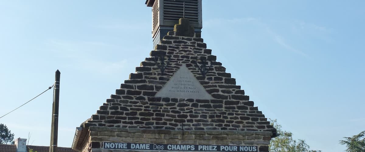 A small stone chapel with a red door and a weather vane on top.
