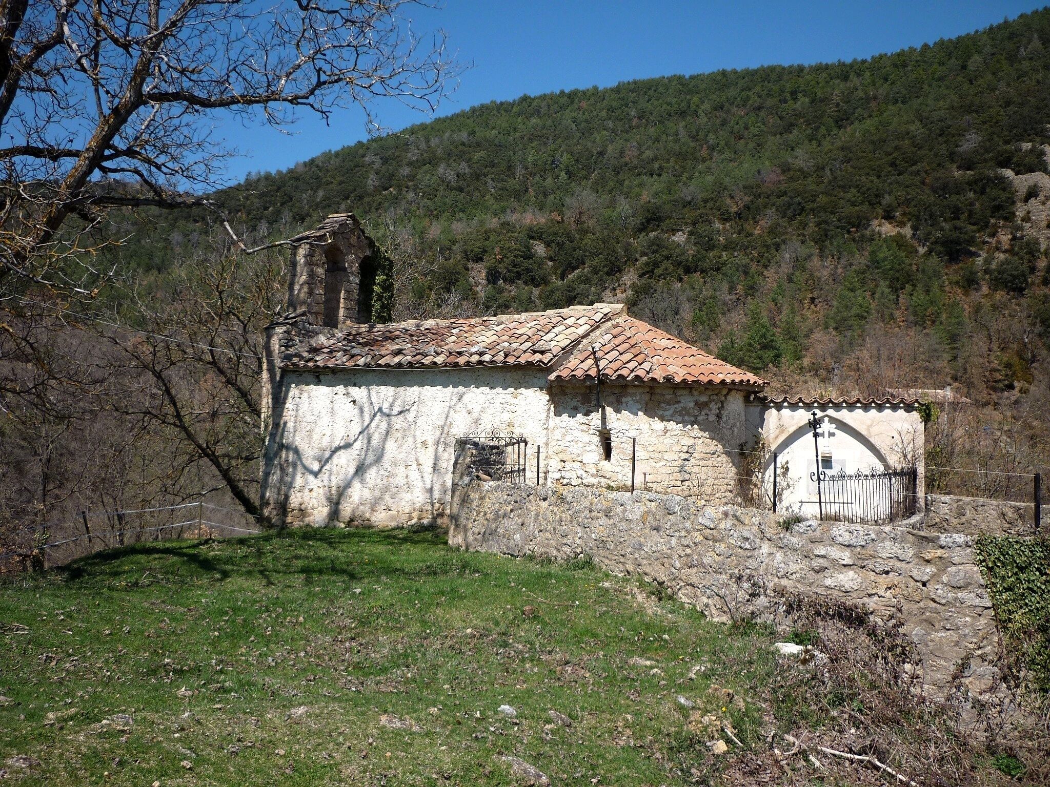 A stone church with a tiled roof, surrounded by a grassy area and a hillside in the background.