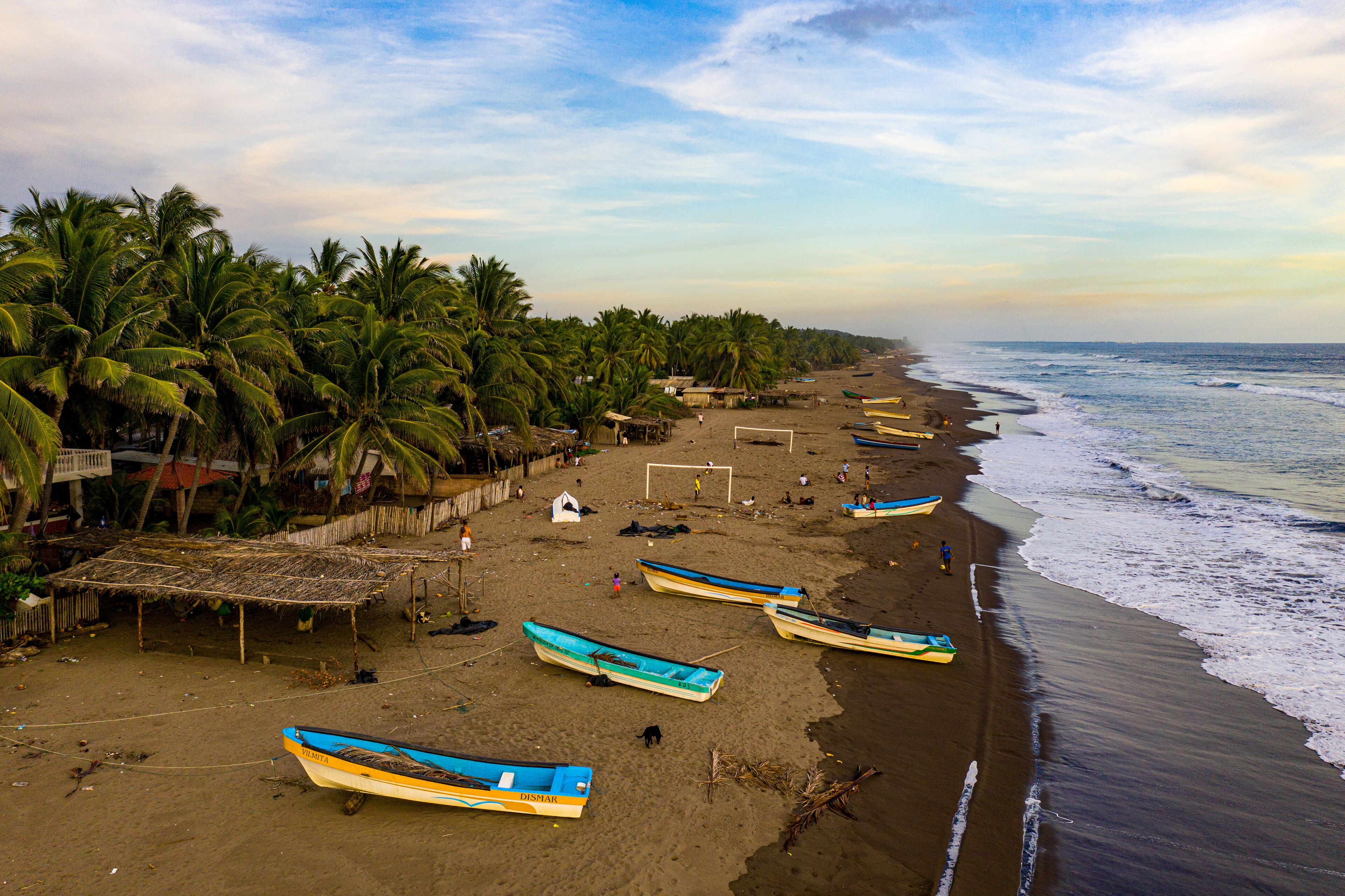 A beach with palm trees, a soccer goal, and several boats.