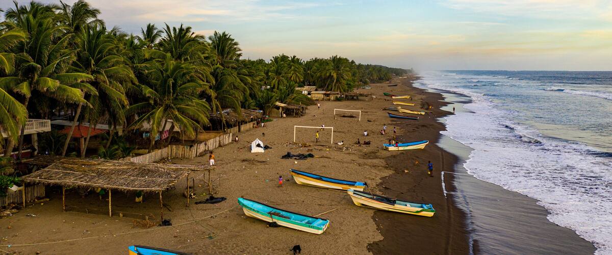 A beach with palm trees, a soccer goal, and several boats.
