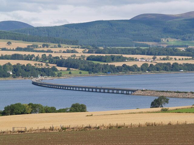 A circular dam with a bridge over a river, surrounded by fields and hills.