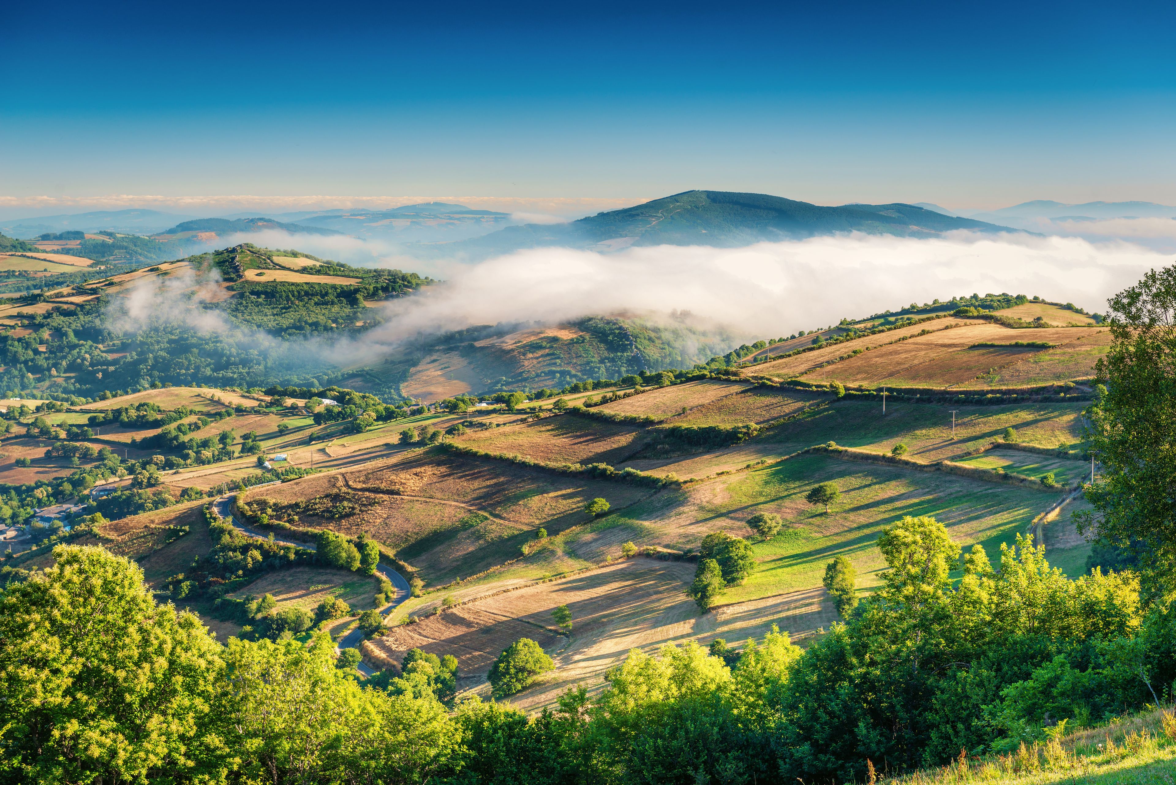 Een bergachtig landschap met glooiende heuvels, velden en een weg die door het gebied kronkelt.