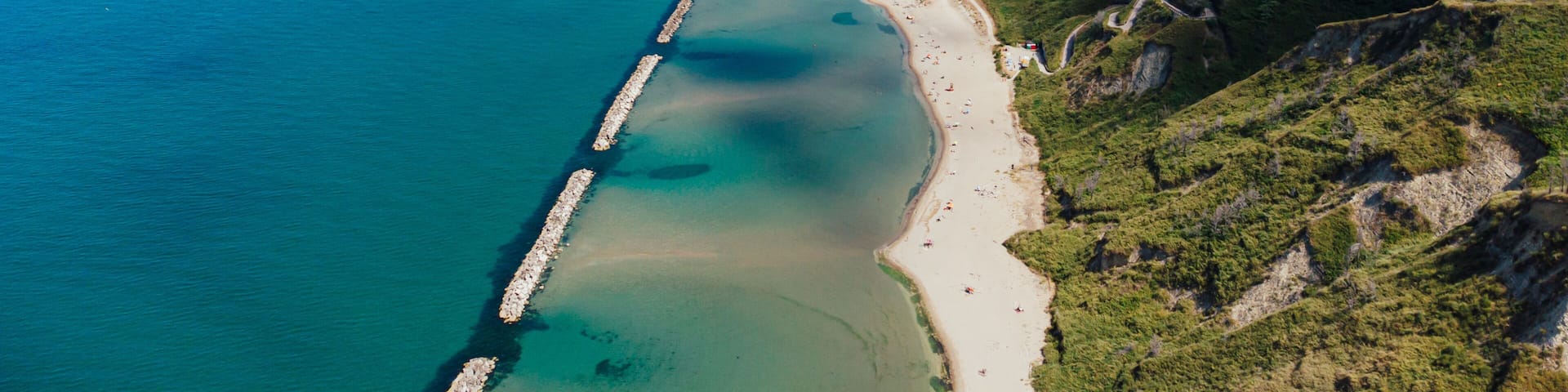 A coastal landscape with a beach, a pier, and a cliffside.