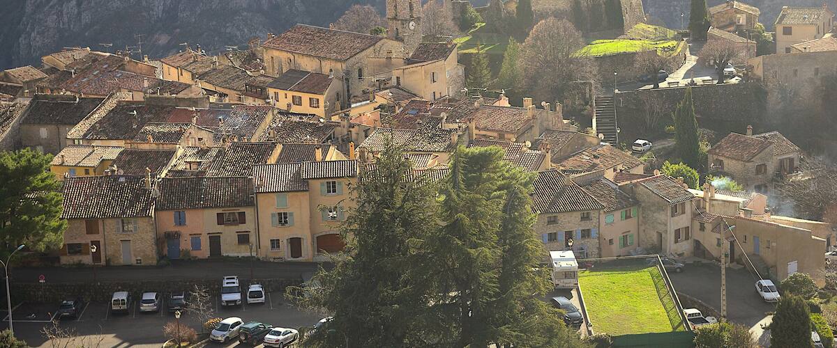 A historic town with medieval architecture, including a castle and church, surrounded by mountains.