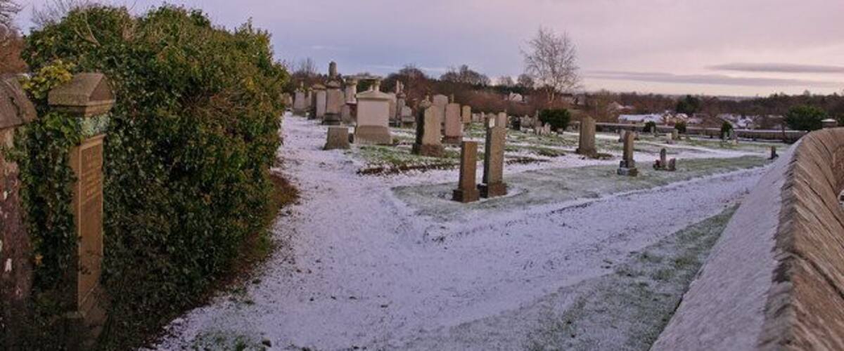 A cemetery with headstones and a snow-covered path.