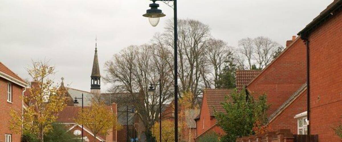 A narrow brick pathway flanked by houses and a church steeple in the background.
