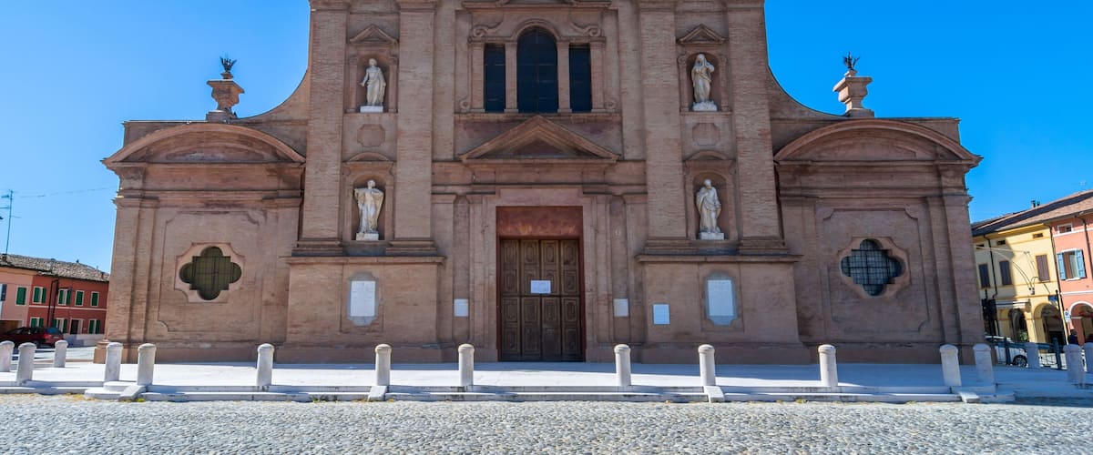 A large, historic church with a prominent entrance, statues on either side, and a clear blue sky in the background.