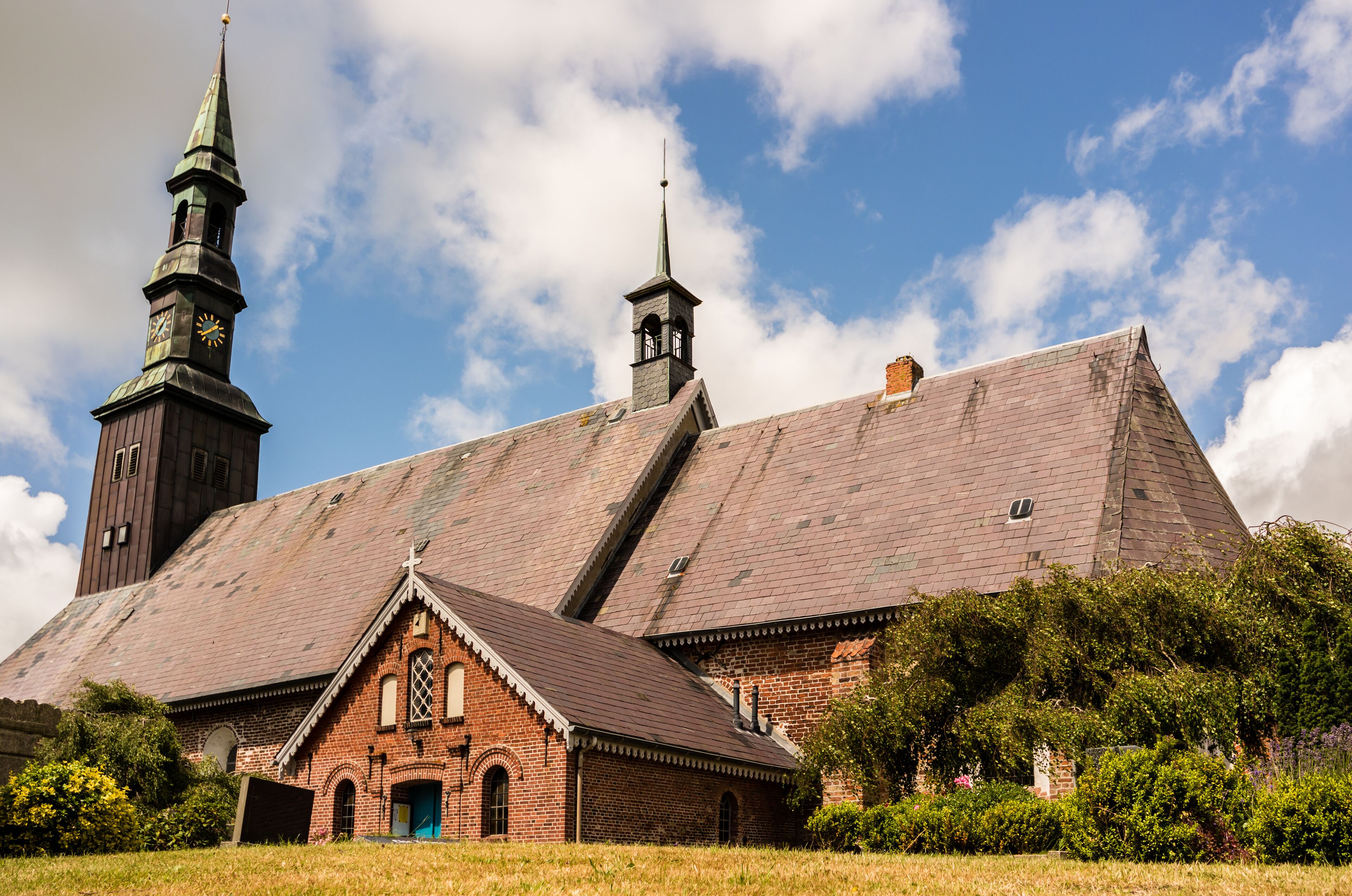 A historic church with a prominent steeple and clock tower, surrounded by lush greenery.
