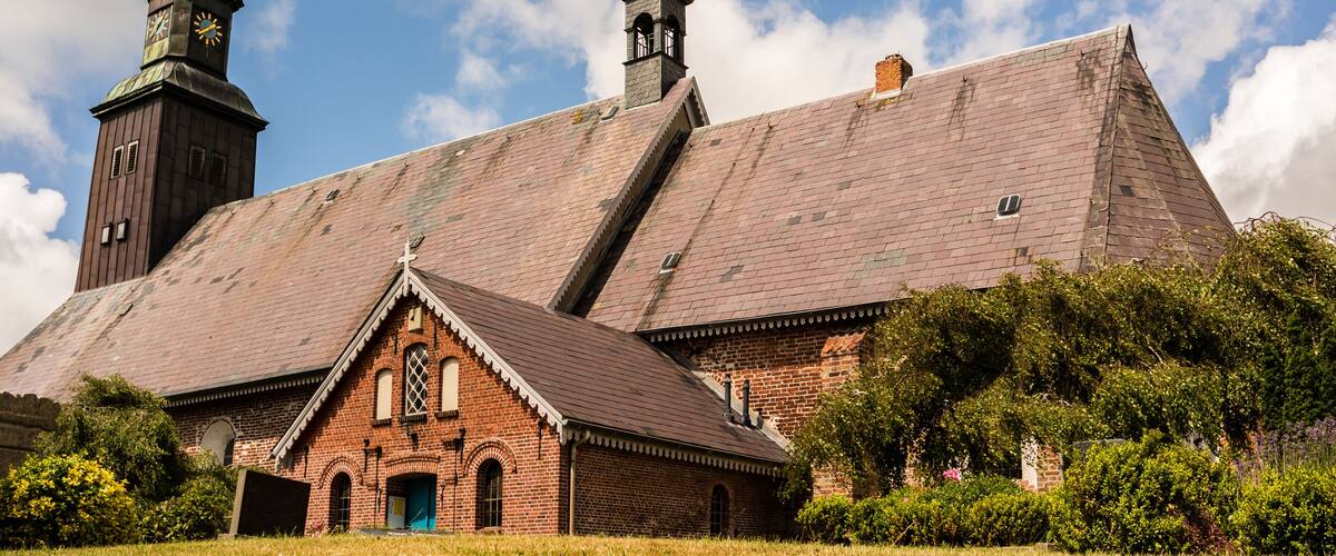 A historic church with a prominent steeple and clock tower, surrounded by lush greenery.