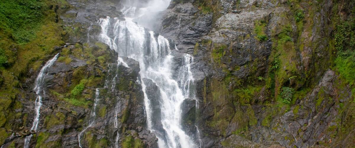 A multi-tiered waterfall cascading down a rocky cliff surrounded by lush greenery.