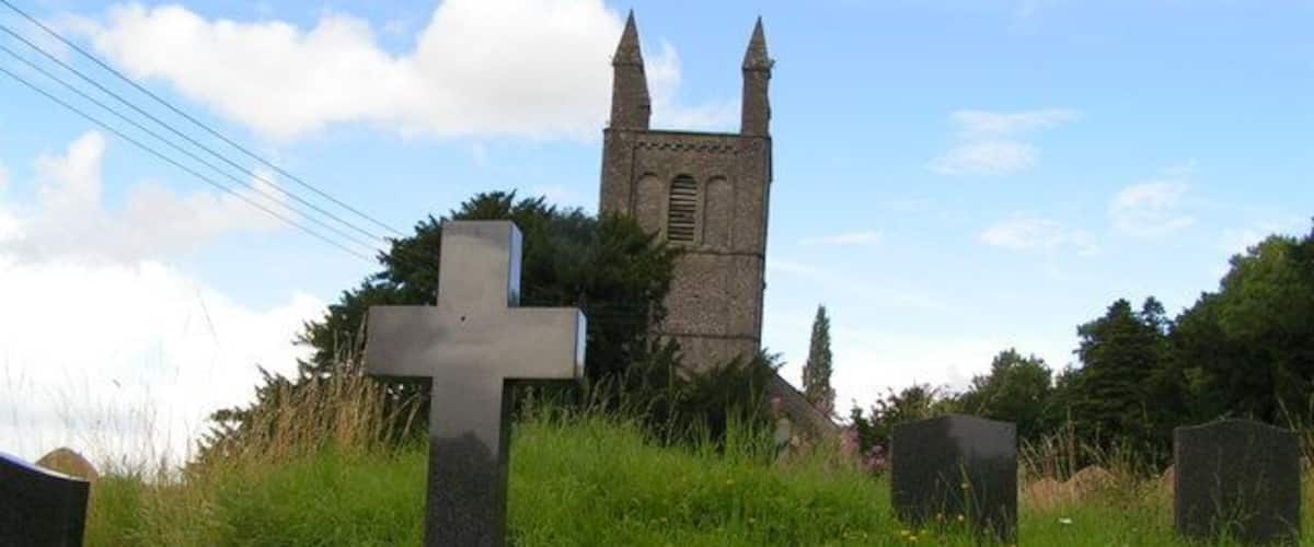 A cemetery with a prominent cross and a church tower in the background.
