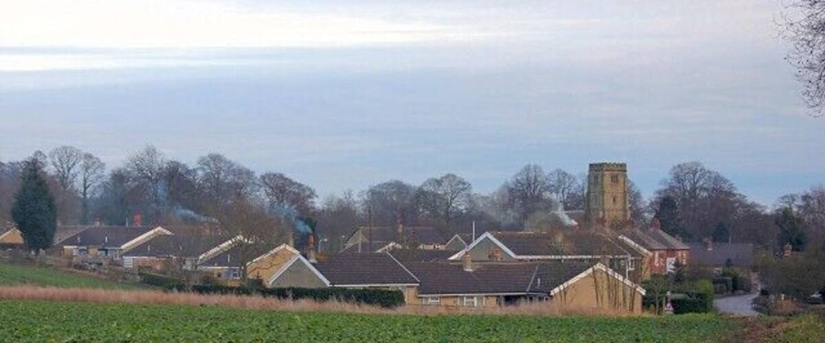 A rural landscape with houses, a church tower, and a field.