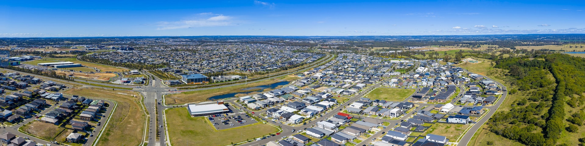 Vista aérea de uma área residencial com casas, ruas e um grande edifício industrial.