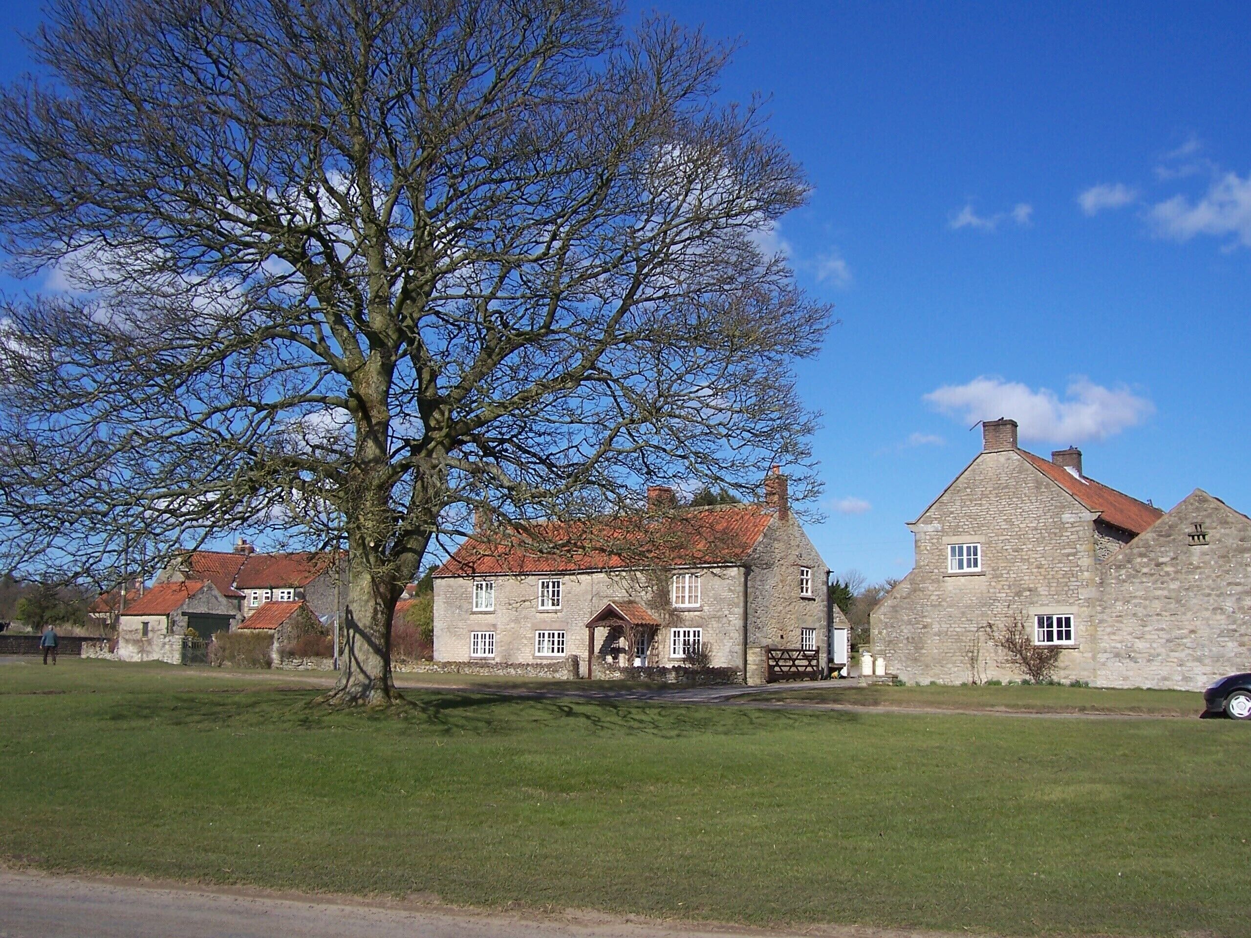 A stone building with a red roof, surrounded by a grassy area and a large leafless tree.