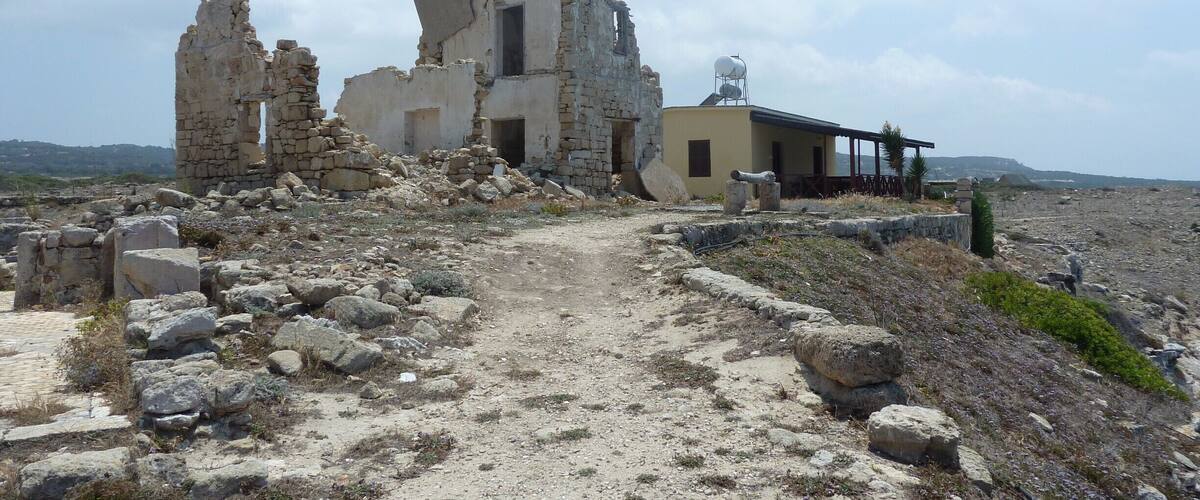Ancient ruins with stone walls and a small building with a water tank.
