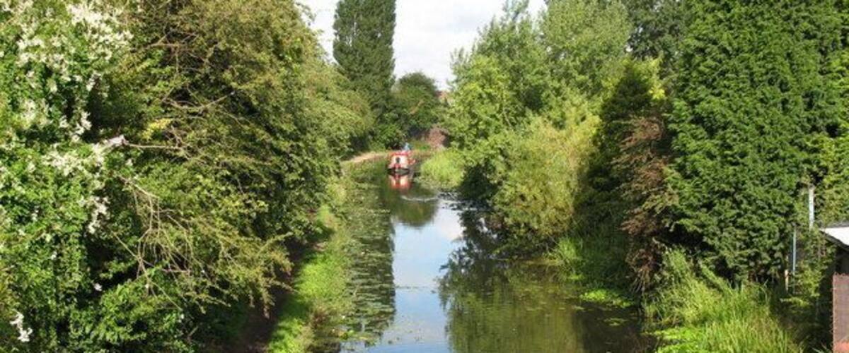 A narrow waterway flanked by dense greenery and a path.