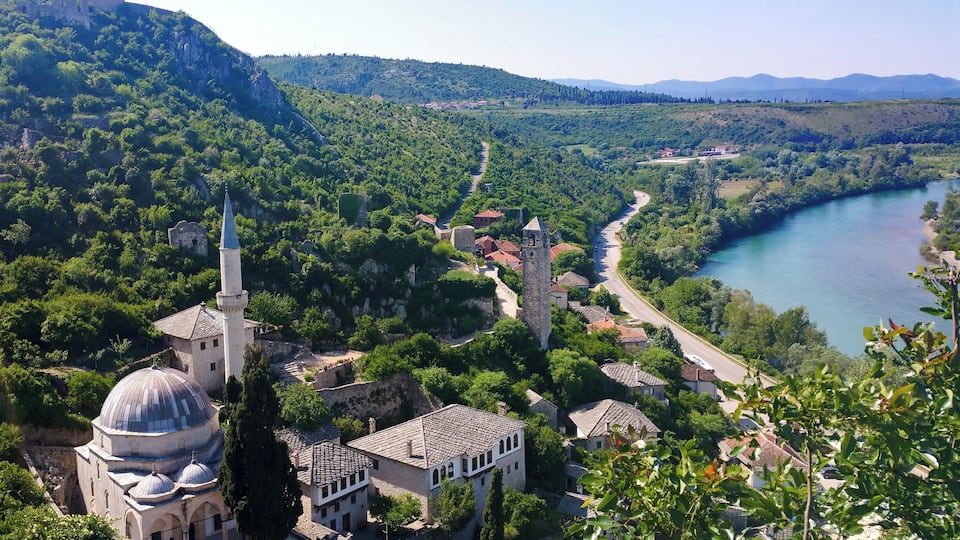 A historic town with a prominent mosque, a river, and a castle on a hill.