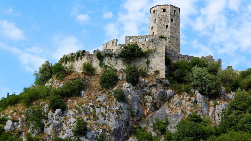 A historic stone castle atop a rocky hill with lush greenery.