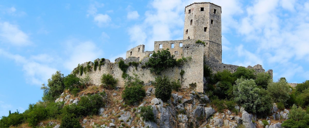 A historic stone castle atop a rocky hill with lush greenery.