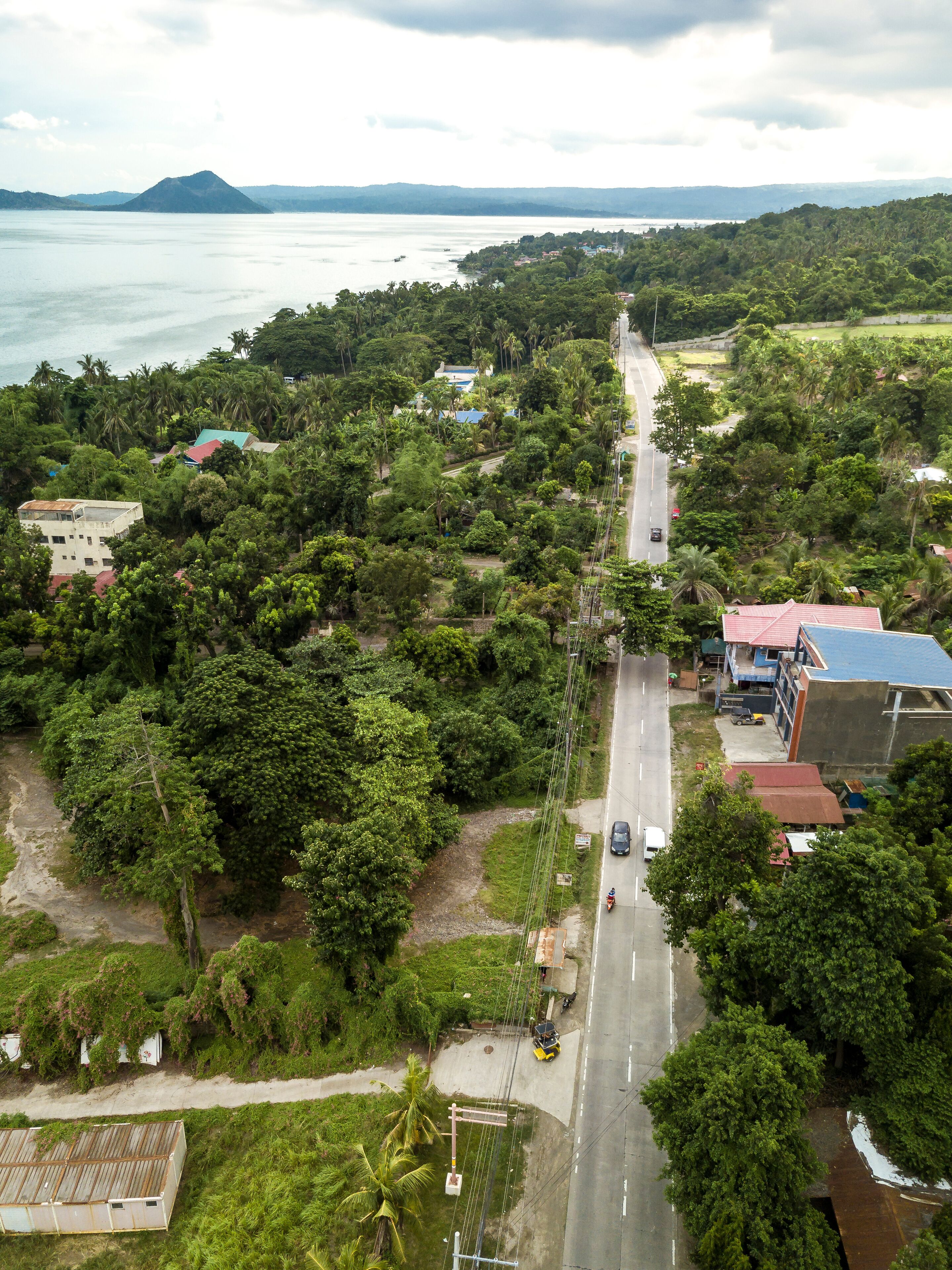 A coastal town with a road running through it, surrounded by lush greenery and a body of water in the background.