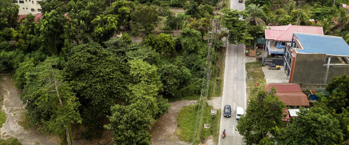 A coastal town with a road running through it, surrounded by lush greenery and a body of water in the background.