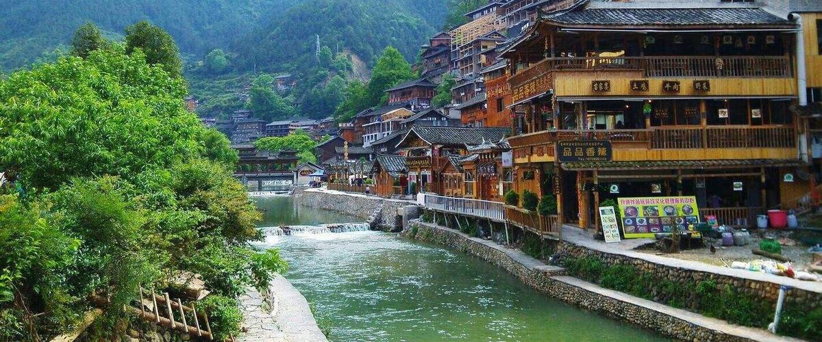 A traditional Chinese village with wooden buildings, a river, and lush greenery.