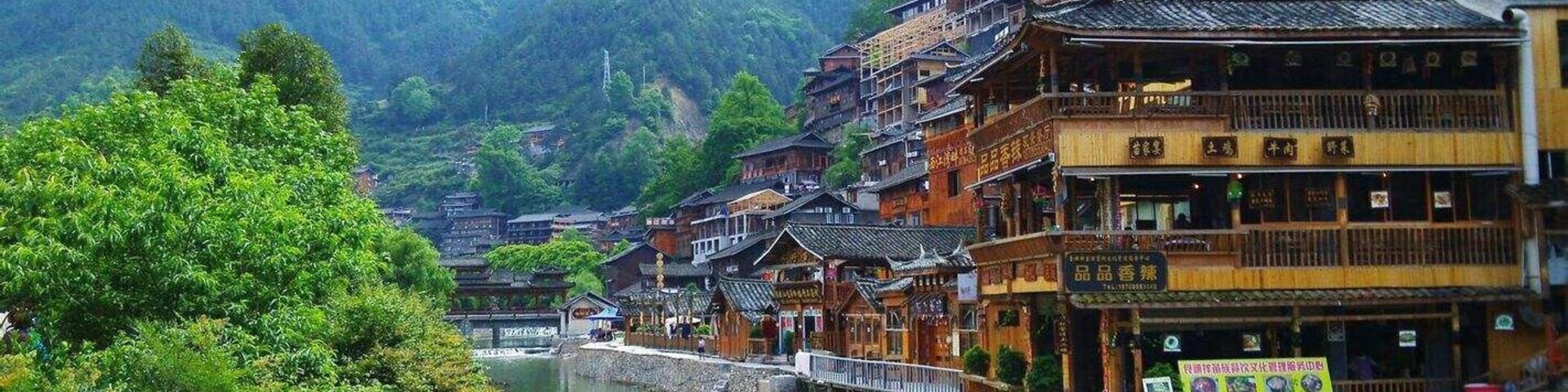 A traditional Chinese village with wooden buildings, a river, and lush greenery.