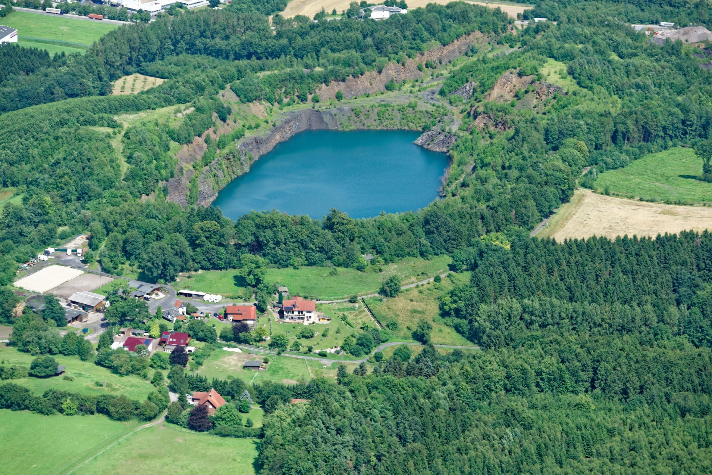 A lake surrounded by dense forest and a small village with red-roofed houses.