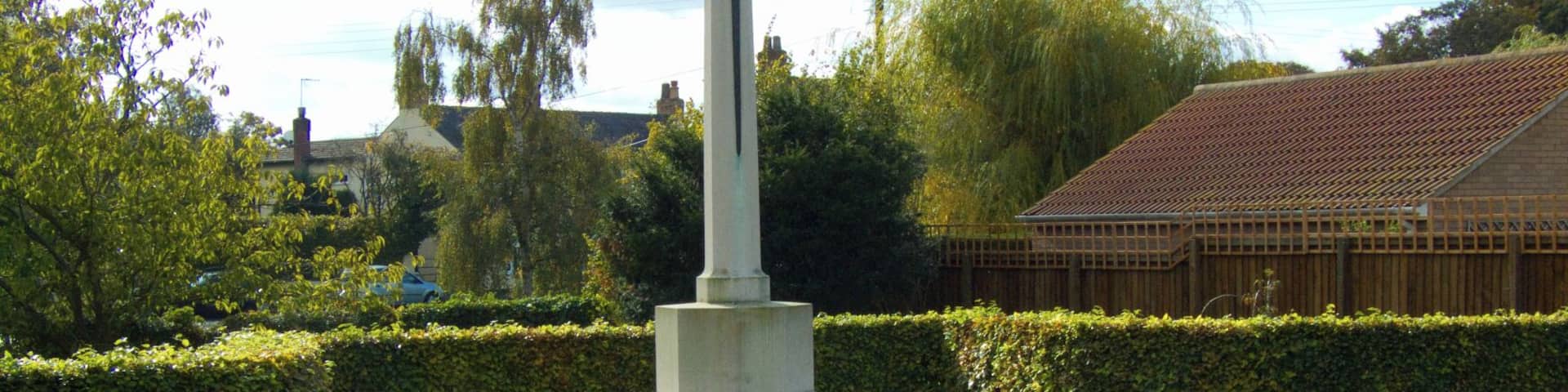 A war memorial with a cross, surrounded by gravestones and greenery.