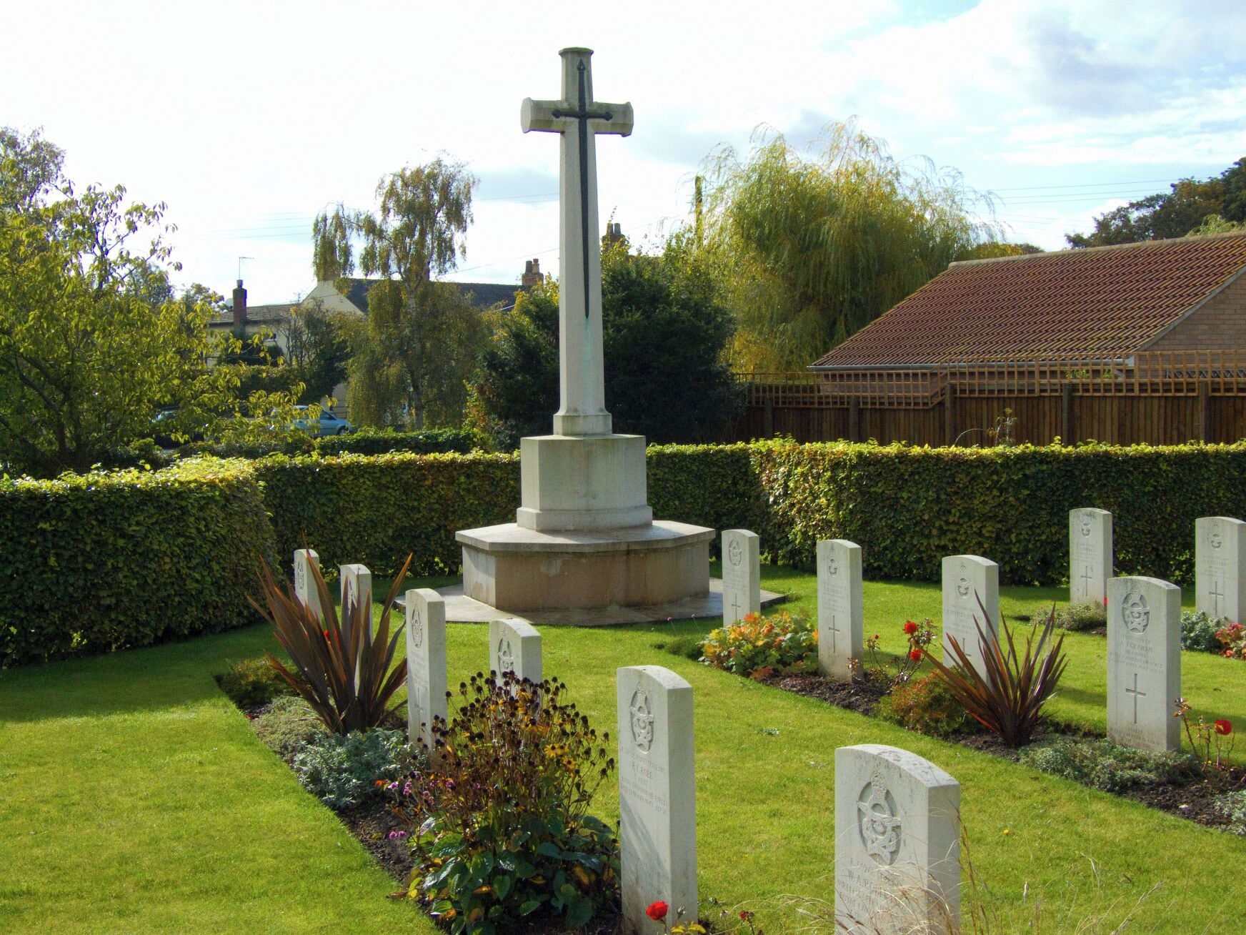 A war memorial with a cross, surrounded by gravestones and greenery.