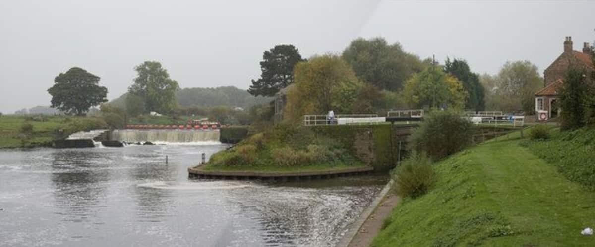 A river with a lock, a bridge, and a house on a grassy bank.