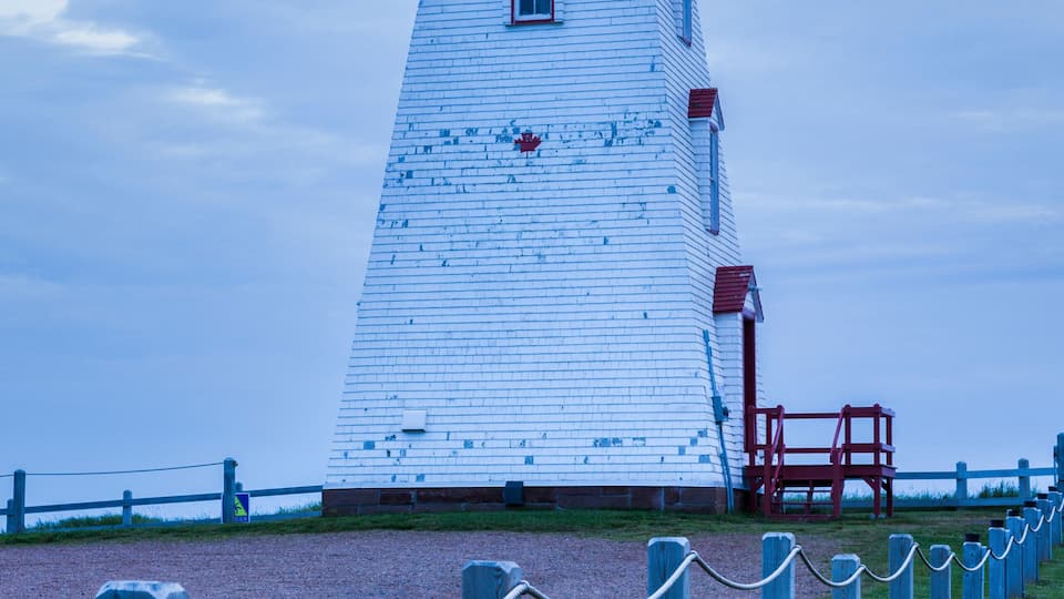 A white lighthouse with a red top, surrounded by a grassy area and a wooden fence.