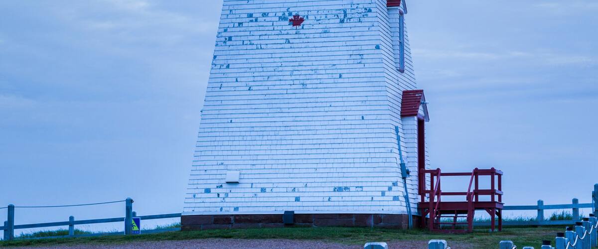 A white lighthouse with a red top, surrounded by a grassy area and a wooden fence.