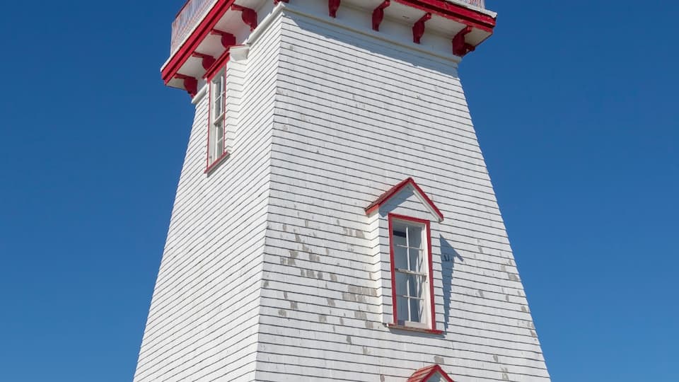 A tall white lighthouse with red accents and a red roof, surrounded by a grassy area.