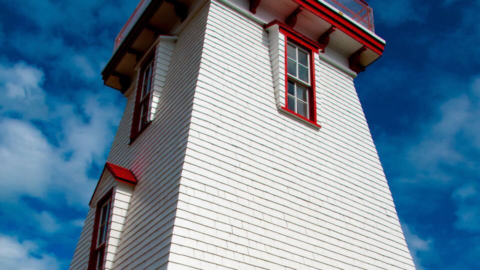 A white lighthouse with red trim and a red balcony against a blue sky.