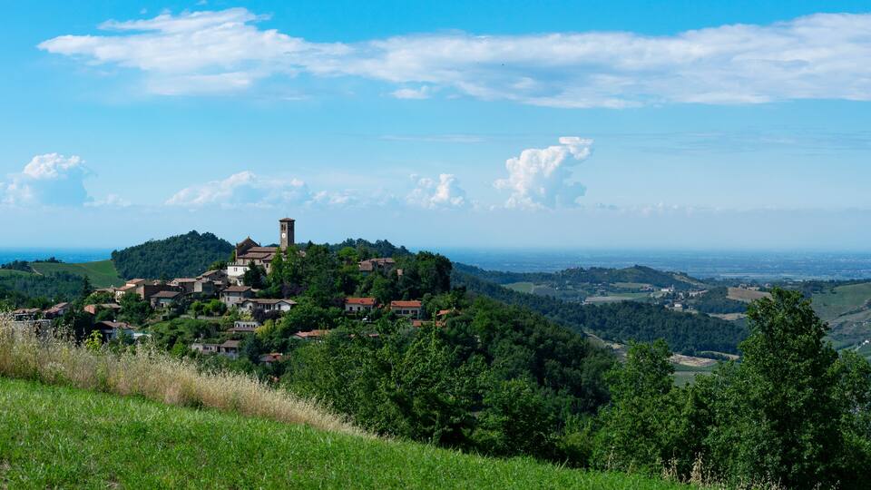 A village on a hill with a church tower, surrounded by greenery and rolling hills.