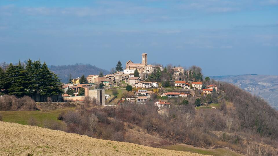A hillside village with a prominent church and clock tower, surrounded by trees and houses.