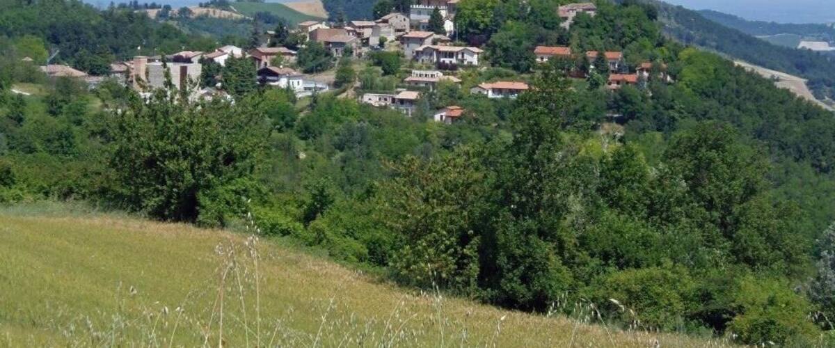 A hillside village with a prominent tower, surrounded by lush greenery and a clear sky.